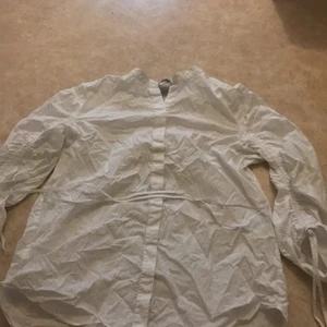Vit blouse  - Säljer denna ish blouse tröja? vet inte riktigt vad det är men den är riktigt gullig! Den har korsett saker längs armarna som man kan spänn åt, man kan oxå knyta runt midjan!