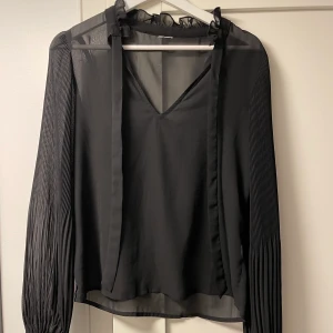 Blus - Svart blus med lite vidare armar i ett lite genomskinligt material med detaljer på armarna. Väldigt bra skick och använd väldigt få gånger. Fint att ha någon gullig topp under. Passar storlek XS/S. Köparen står för frakten.