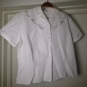 Vintageblus - Vit vintageblus med spets detaljer. Kort modell att ha nedstoppad i byxor🌻