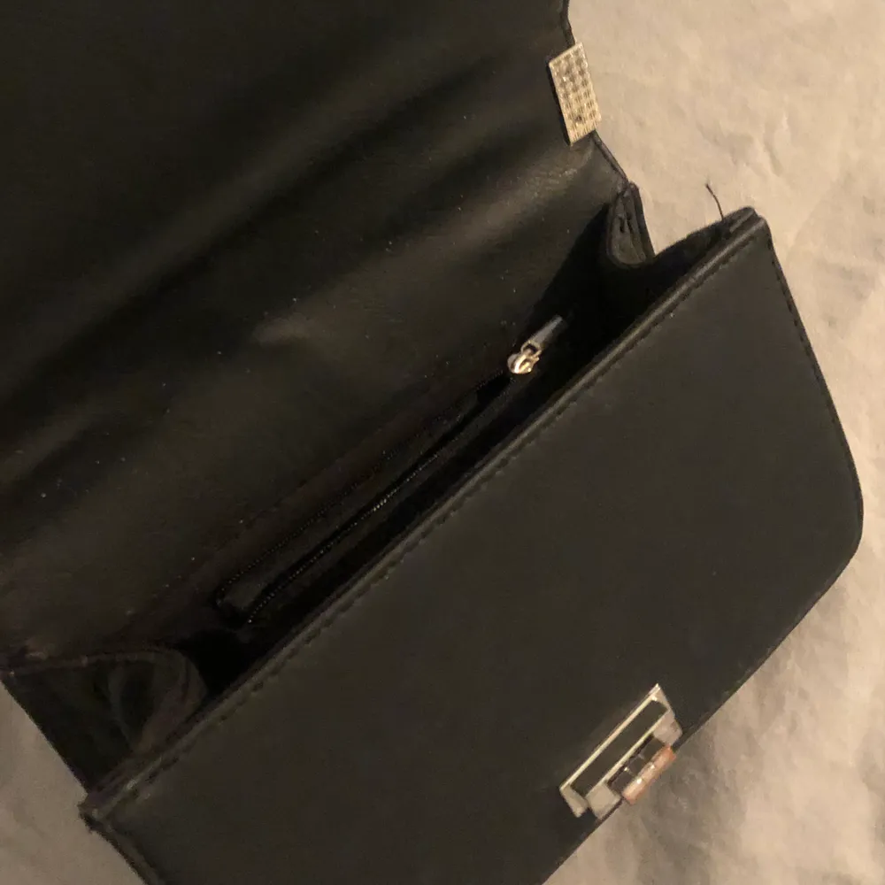 Det här är en väska i svart fake skinn och med silvriga detaljer. Det silvriga spännet är lite missfärgat. Den är från Ur&Penn . Väskor.