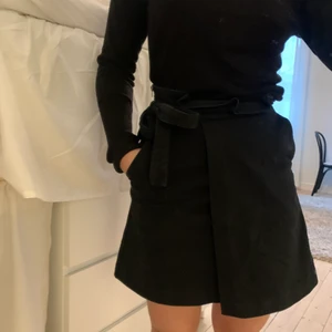 Svart omlottkjol - Svart omlottkjol i grövre ”kostym”-material från H&M. Dragkedja, knytning och FICKOR. Stl.34. 