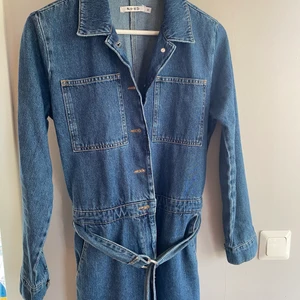 Jeansjumpsuit från Na-Kd, storlek 38 - Jumpsuit i jeans, raka/vida ben och bälte i midjan. Perfekt längd på mig som är 168cm lång. Aldrig använd, endast testad.