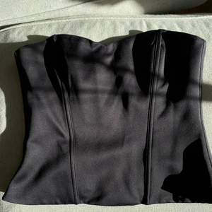 Svart korsett - Svart korsett i sidenmaterial. Storlek 40, men kan passa en 38a lika bra. Speciellt om man har större byst. Plagget mäter 77cm i midjan (omkretsen).