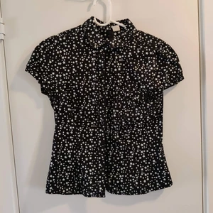 Kortärmad blus - Fin kortärmad svart blus med vita stjärnor. Bröstficka på vänster sida.