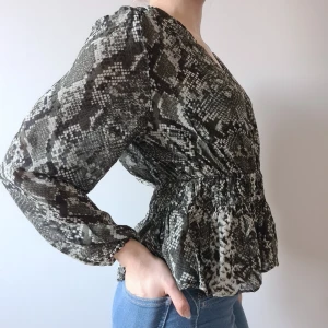 Ormskinsmönstrad blus med volanger - Skön ormskinsmönstrad grön luftig v-ringad blus med volanger nertill & resår som ger en smickrande midja. Frakt tillkommer med 48 kr (ej spårbart brev). Hittar du fler varor så samfraktar vi. :)