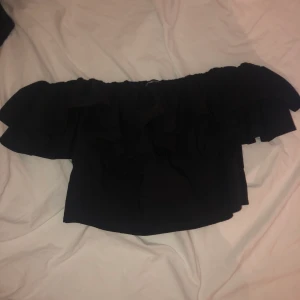 En svart topp - En svart off shoulder topp med volang ifrån Gina tricot i str 42, den passar dig som vanligtvis har str 36/38. Köparen står för frakt 