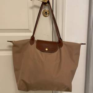 En beige Longchamp väska i använt skick med fläckar, ännu lite fler på undersidan också. Köpt för 1450kr💓(ÄKTA)