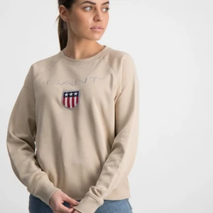GANT Sweatshirt  - Fin Sweatshirt från GANT i fint begagnat skick och endast använd ett fåtal gånger. Tröjan har en beige nyans och en normal passform med rund halsringning. Loggan är broderad och under den sitter en patch med den klassiska skölden. Matcha gärna denna tillsammans med ett par jeansshorts eller jeans. -Sweatshirt  -Broderad logga  -Rund halsringning  -Muddar i midja och vid ärmslut.  -Normal passform  -Färg: 277 Dry Sand  Material: 87% Bomull och 13% Polyester.              Ordinariepris: 699:- /st 