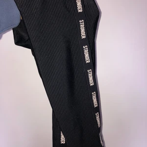 Ribbade Stronger byxor - Ett par ribbade glansiga träningsbyxor från Stronger som har används en gång. De är i fint skick och är jag skulle säga att de är mid rise/hige rise i midjan.