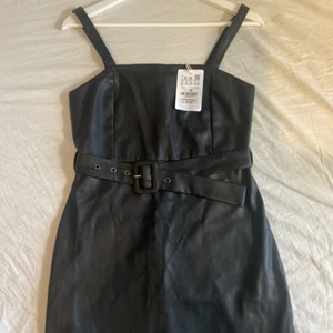 Klänning - Svart klänning i läder/skinn imitation med skärp, från Pull&Bear. Helt oanvänd med prislappen kvar, endast provad. Säljer pga att den aldrig kommer till användning.