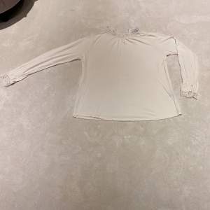 En vit tröja med fina detaljer vid kragen och slutet av ärmarna.