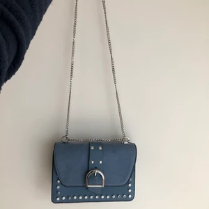 Handväska blå topshop  - Blå mindre handväska från topshop. Använd fåtal gånger så ser helt ny ut, inga skador eller märken. Delvis mocka imitation/skinn. Handtaget är en kedja som du kan göra lång så du kan ha den över axeln och kort att hålla i handen eller på ena axeln. 