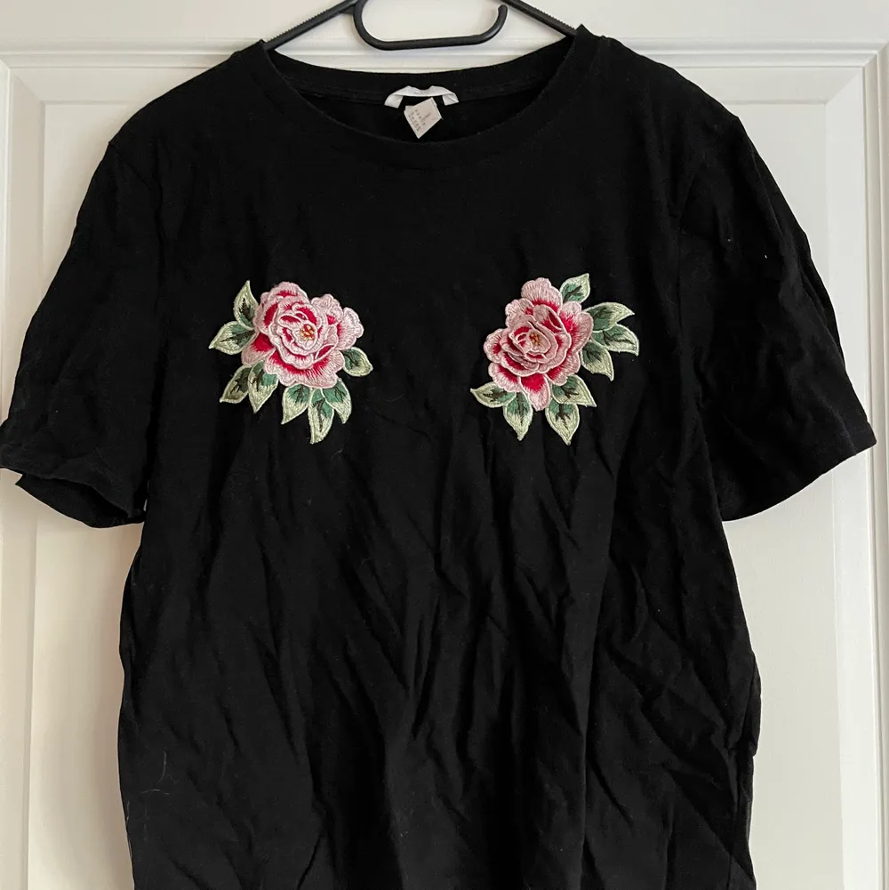 En svart T-shirt med två rosor på bröstet. Lite skrynklig dp den legat i en låda för länge så nu är det dax för en ny ägare! . T-shirts.
