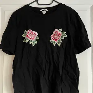 En svart T-shirt med två rosor på bröstet. Lite skrynklig dp den legat i en låda för länge så nu är det dax för en ny ägare! 