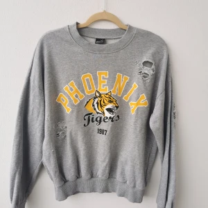 Sweatshirt Strl S - Riktigt cool sweatshirt med slitna hål. Givetvis meningen dom ska vara där. Grå botten med gul text och tiger på. Strl S. 150kr eller Bud. Köparen står för frakten och jag tar alltid 2 kr för emballage. 