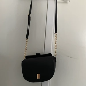 Svart axelväska - Säljer en svart axelväska med guldiga detaljer. 20cm hög och 22 cm bred 