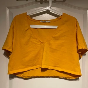 Gul croptop  - Senapsgul kort T-shirt med djup vringning från na-kd. Köparen står själv för fraktkostnaden.