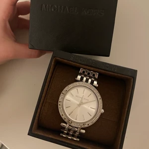 Michael Kors Klocka - Äkta silvrig Michael Kors Klocka med silvriga diamanter. Säljer pga av att de har lossnat några diamanter men går fortfarande att använda!            Frakt tillkommer. 