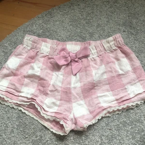 Rutiga Pyjamasshorts  - Rosa rutiga pyjamasshorts med en rosett från Kappahl, storlek 170 så jag skulle säga att de är en XS. De har spets nertill och glittriga linjer vid rutorna, något noppriga men ett skönt och luftigt material. 40kr + frakt🌸🤍