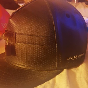 Cayler&sons  - Snygg keps i svart skinn med ett litet hänglås fram och nyckeln på sidan:) den är som ny. 