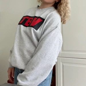 Swetshirt med tryck  - Skittsnygg grå sweatshirt med ett svårt tryck och röda bokstäver där det står T B V. Trycket är lite slitet och därför går den ner i pris. Den är i storlek L och jag är storlek s/m. 