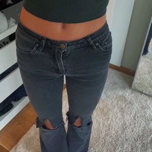 Lågmidjade jeans  - Svarta/gråa lågmidjade jeans med två egengjorda hål på knäna. Strl 26/32 men de är i ett väldigt stretchigt material. De är ganska använda och har små små hål på rumpan, men inga stora defekter. 