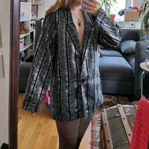 Silver randig Kavaj / Kappa / Klänning 38 - Riktigt snygg kavaj / kappa i storlek 38. Mäter 76cm under kragen och ner.📏 Kan även användas som klänning eller oversized jacka om man är mindre. Tunnare glansigt tyg med blommor🌸 Något vikt i ärmarna då jag rullat upp dem, men det går bort när man stryker<3 Perfekt till festligare tillfällen! Säljes då den inte kommer till användning längre. Har ficka på båda sidor👑