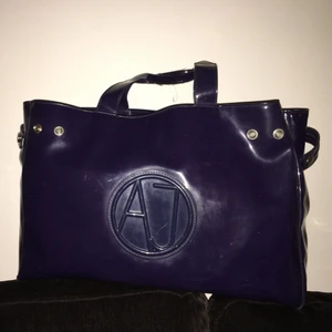 Armani jeans handväska .AJ - Armani jeans handväska i lila färg och en dust bag. Vaska är av pvc-plasten .väska model är  Armani Jeans diamond shopper bag. Toppskick och rent.40x 28x 12 cm