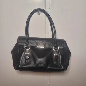 Guess handväska - Guess handväska med lite slitage på metallen och på kanterna av väskan(se bilder). Även ett axelband som aldrig använts hänger med.  34×18×18cm