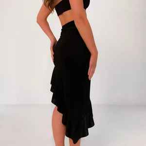 Topp och kjol  - Plagget är inte använd! En bandeau-topp i ett stretchmaterial ihop med asymmetrisk midikjol med volanger.                                                NOTERA!! Vid leverans av varan (för de som inte bor i Göteborg) blir priset annorlunda (lägre). Diskuteras med köparen.