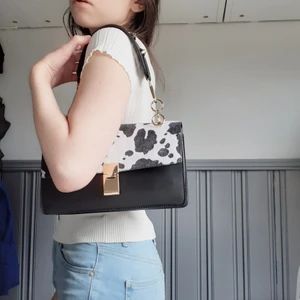 Axelväska - Komönstrad väska som är slutsåld på Ginas hemsida! Den mönstrade delen är i lite pälsaktigt material. Endast använd 1gång och därav i nyskick!❤Medföljer även ett svart längre tillhörande väskband(väskbanden är avtagbara). Frakt tillkommer på 50:-😘