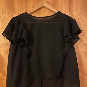 Fin tröja svart - Finare tröja med små knappar där bak. Korta armar med volanger. Storlek xs från monki. Luftigt material sitter bra knappt använd. 