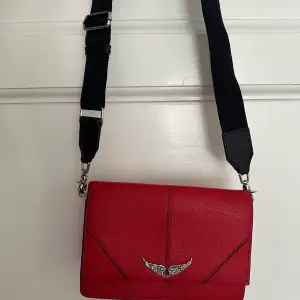 Röd Zadig&Voltaire väska väldigt sparsamt använd. Inköpt 2020 i Spanien för 295€ (se bild, kvitto finns). Brett axelband med logga. Pris 1000kr. 