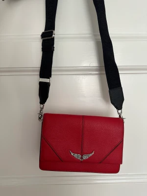 Zadig &Voltaire handväska  - Röd Zadig&Voltaire väska väldigt sparsamt använd. Inköpt 2020 i Spanien för 295€ (se bild, kvitto finns). Brett axelband med logga. Pris 1000kr. 