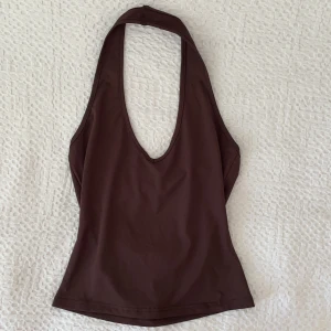 Brun halterneck  - Säljer denna bruna halterneck som är figursydd och formar sig jättefint på kroppen! Den har ett badräktsliknande material och sitter tajt åt! Storlek 36 och passar mig perfekt som har S. Är i bra skick!