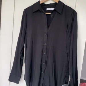 Svart satinskjorta - Använd 1 gång därmed nyskick. Svart mjuk skjorta i satinimitation. Något oversized