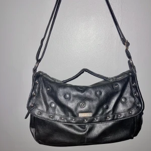 Y2k väska med nitar - Daniel Ray väska från 2000 talet. Mellanstor med nitar, spännen ock många fack. Frakt tillkommer.