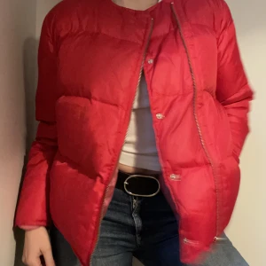 Acne studios dunjacka - Populär dunjacka från Acne studios. Röd med rosa innefoder och något längre baktill. Jackan har täcken på användning då den har en liten reva på ena ärmen (se bild) samt att den skulle må bra av en kemtvätt.  Nypris ca 2500 kr Mitt pris 1000 kr