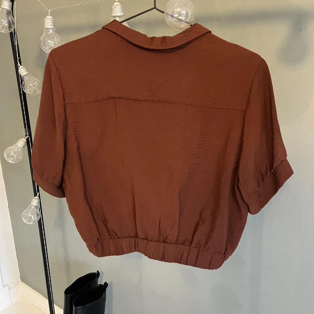 Croppad skjorta med korta ärmar från Monki i en rostbrun färg. Använd 1 gång. Köparen står för frakten🫶🏼. Toppar.