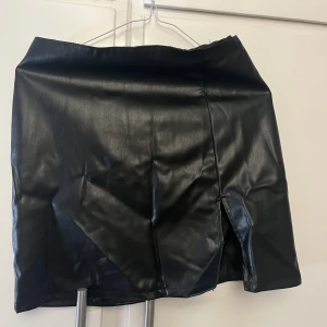 Kort kjol - Svart kjol i läderimitation. Dragkedja på baksidan och en liten slits på framsidan