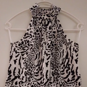 NY, oanvänd svart - vit halternecktopp / topp med polo. Storlek: 34/XS. - Helt NY och oanvänd svart/vit djurmönstrad halternecktopp/ärmlös topp med polo. Knäpps bak i nacken. Storlek: 34/XS. Material: Mjuk, behaglig bomull. Helt felfri.