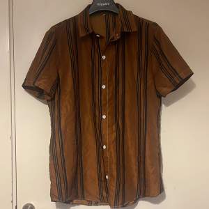 Brun färgad skjorta med linjer, ger lite av en malibou feeling. Skön material och är i medium storlek. 