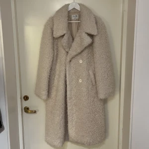 Vit kappa i teddy - Vit kappa i teddymaterial från NA-KD, storlek 38.