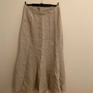 Lång linnekjol  - En lång beige linnekjol som är lågmidjad och är 00 talinspierard. Funkar perfekt till ett linne.
