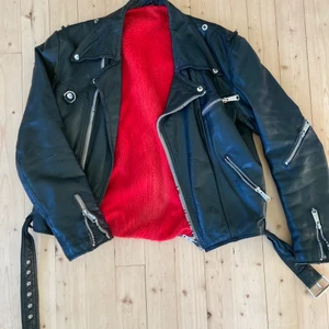 Skinnjacka biker strlk S/M - En vintage biker skinnjacka med rött plyschfoder. Riktigt skön och mjuk i lädret.  Axel - Axel 50cm Arm övre mått 59cm Armhåla - armhåla 59cm Axel - botten 54cm Nacke - ryggslut 59cm  Dragkedjan fungerar inte.  Kan skickas!  Uppskattar strlk till S/M 