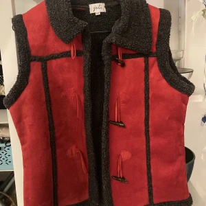 Väst fårskinn mocka - Sååååå ball väst i röd mocka med fårskinnskrage. Duffelspännen. Utmärkt skick. Ball att ha utanpå jackor. Säljer även den röda skinnjackan i annan annons. 