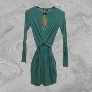 Klänning för utekvällen - Jättefin turkos klänning med twistad front som knyts där bak. Slätt material. Tight modell, både längs kropp och armar. Går till mitten av låren ungefär. Helt oanvänd med lappen kvar.