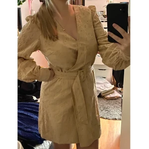 Beige omlott klänning NA-KD  - Beige omlott klänning från NA-KD i storlek 36. Sitter jätte fint och är väldigt vacker. Känner sig lite som en neutral prinsessa :P. Mönster i tyget. Bälte i midjan.