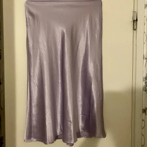 Lila, glansig satinkjol - Superfin satinkjol. Använd bara en gång. Har en fläck på.