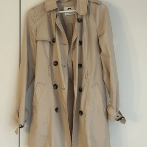 Beige vår-kappa stl 34 - Beige kappa med knappdetaljer från Cubus! Använd fåtal gånger därav att den säljs. 